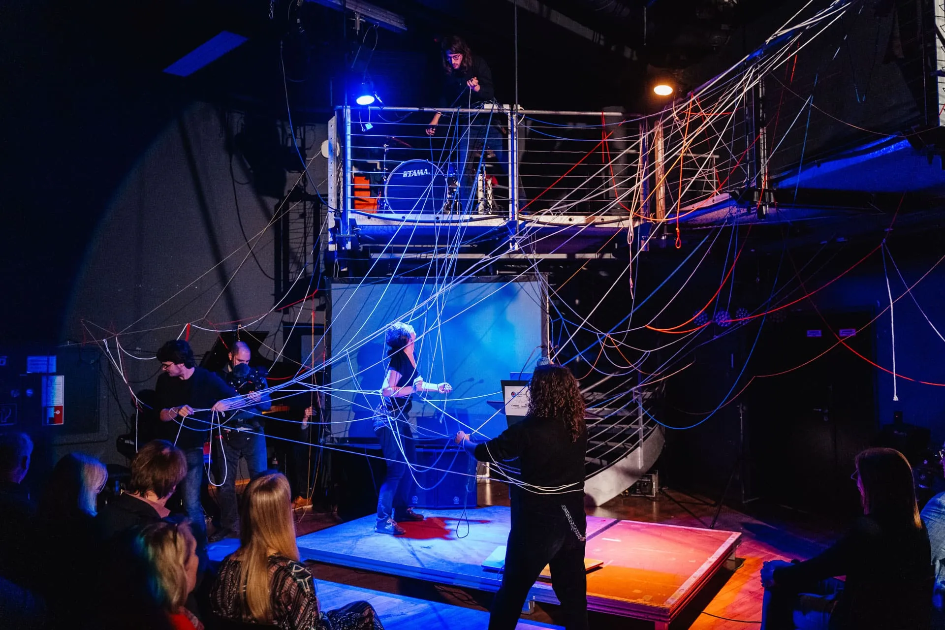 Theaterbühne mit Schauspieler:innen, die Fäden verwirren